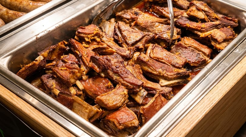 Close-up of a metal serving tray filled with glistening, cooked short ribs, ready to be served.