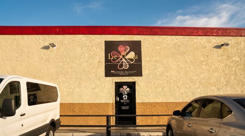 Le U'u restaurant exterior with a black sign, door, and two cars parked outside.